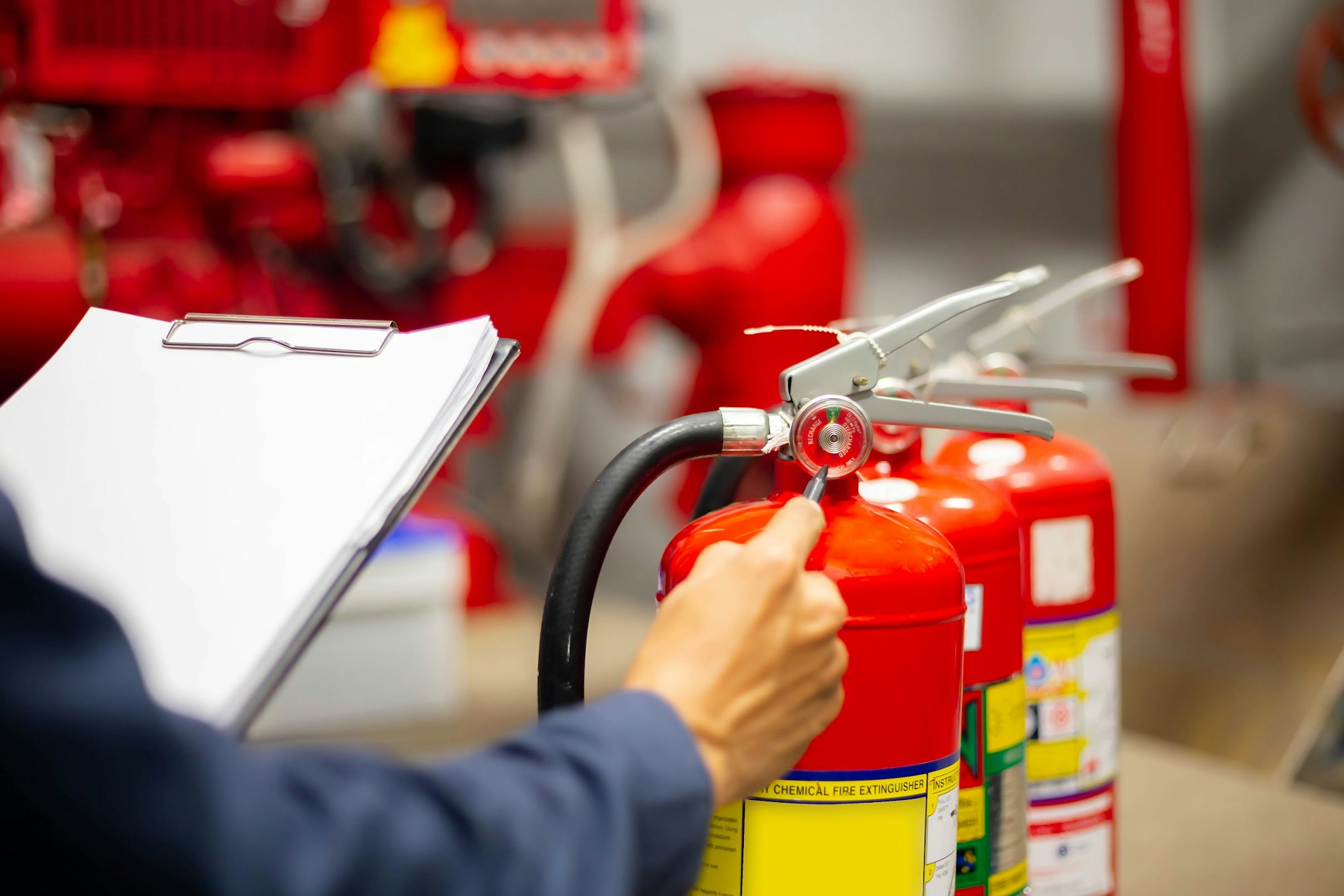 A person inspects fire extinguishers while holding a clipboard, ensuring safety equipment is in good condition.
