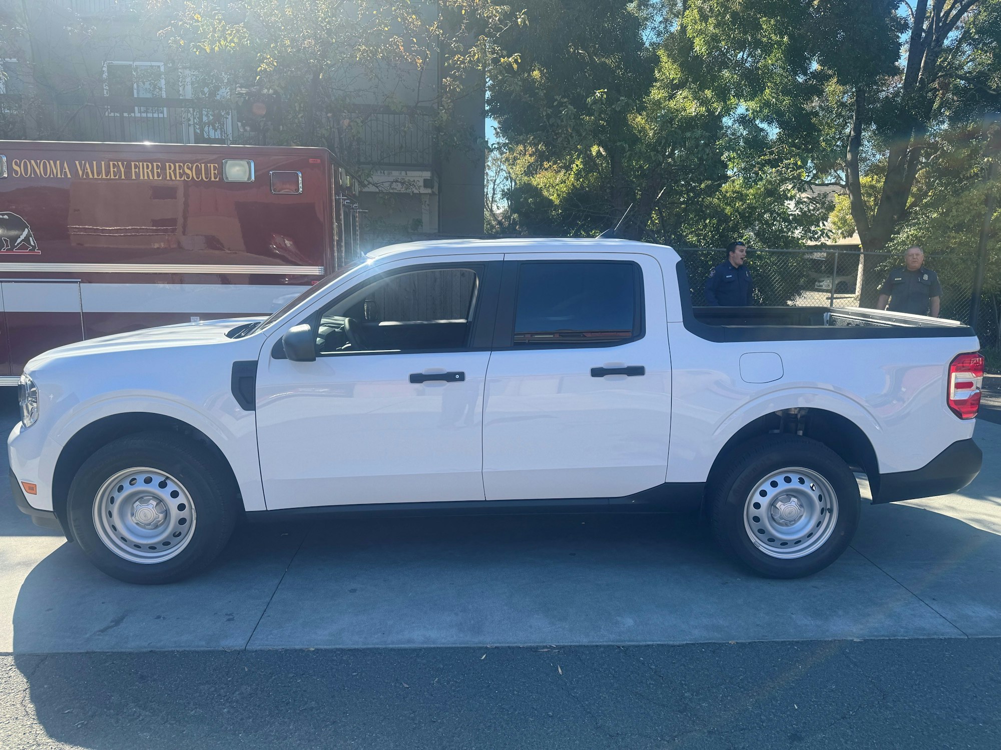 A white pickup truck parked next to a fire rescue vehicle, with two people standing nearby.