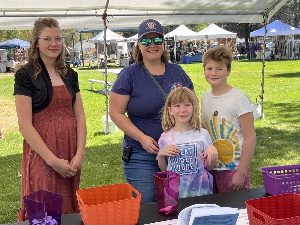 Four people standing at an outdoor event with tents in the background and colorful baskets on a table.