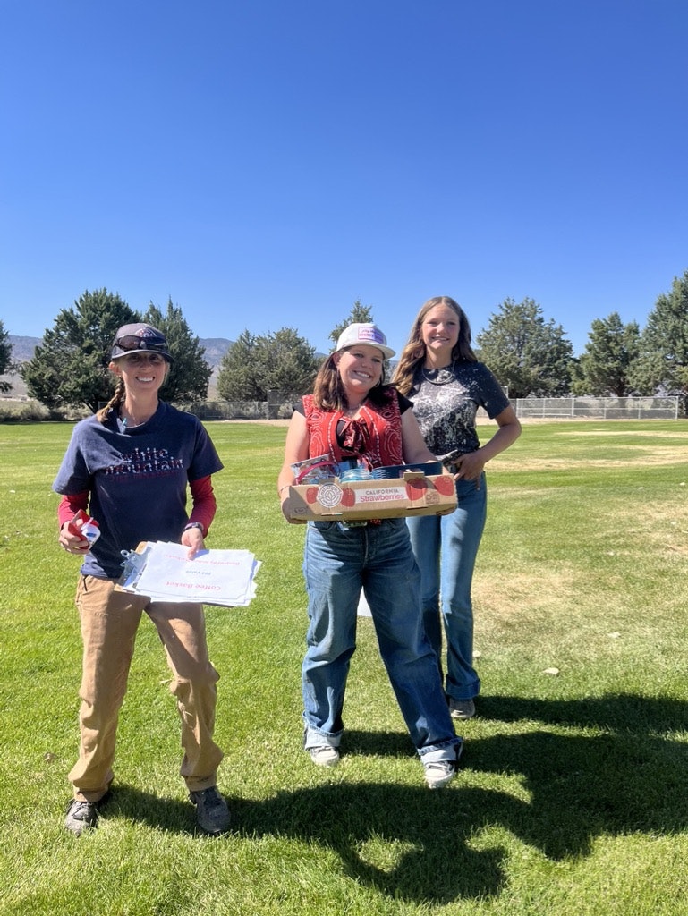 Three people with pizza boxes in a sunny park.