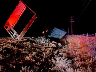 An overturned red truck with its cargo scattered at night, under red and blue lights.