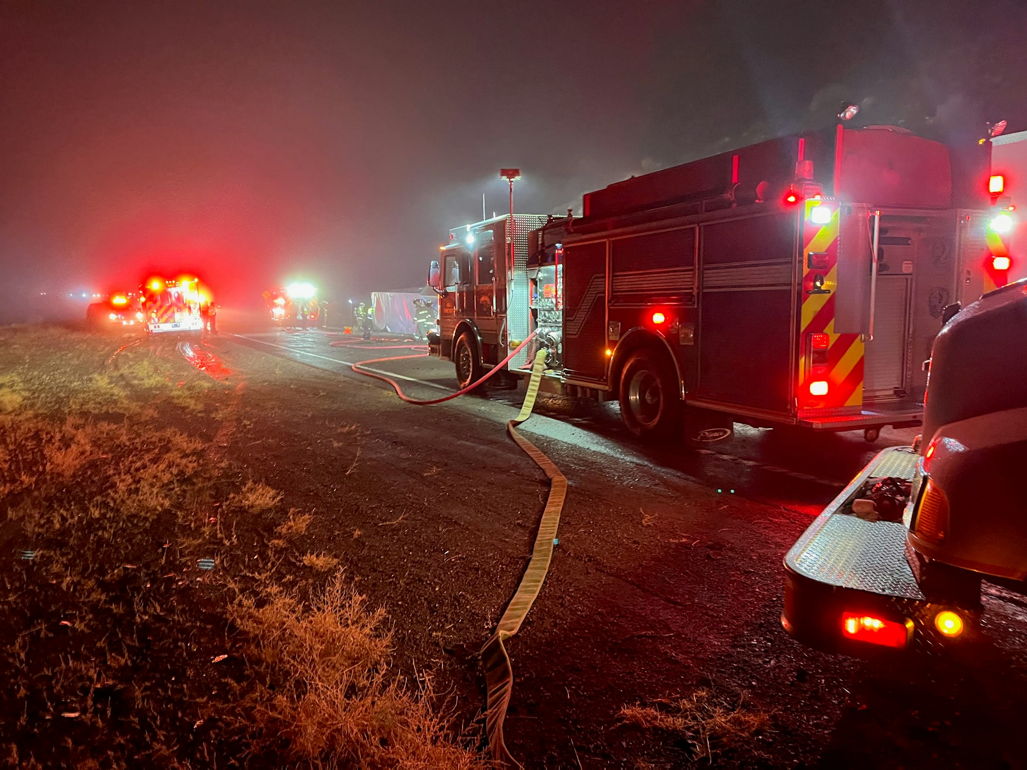 Fire trucks with hoses extended, emergency lights on, at a nighttime scene.