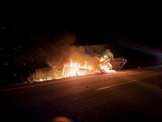 A vehicle on fire at night by the side of the road.