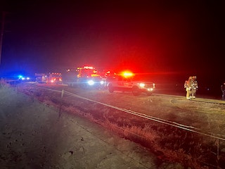 An emergency scene at night with flashing lights, emergency vehicles and personnel, possibly near a road.