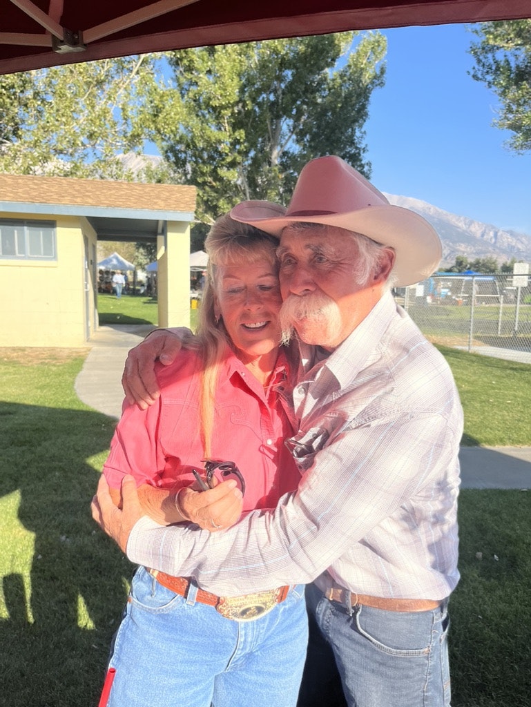 An older couple in cowboy hats sharing a tender moment with the man kissing the woman on her cheek.