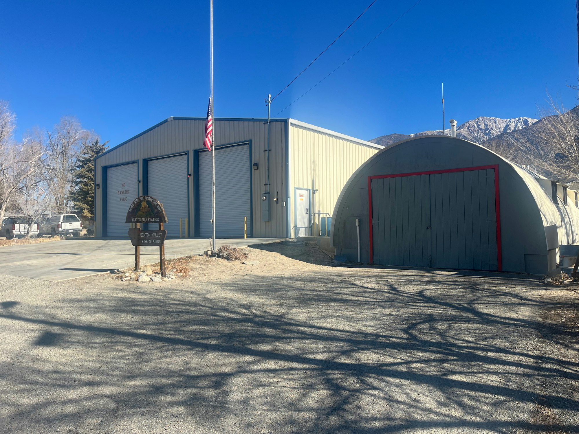 A fire station with a flagpole, mountains in the background, and a curved-roof building.