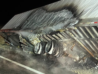 Overturned truck trailer at night; cargo spill, visible damage, wheels up, on road.
