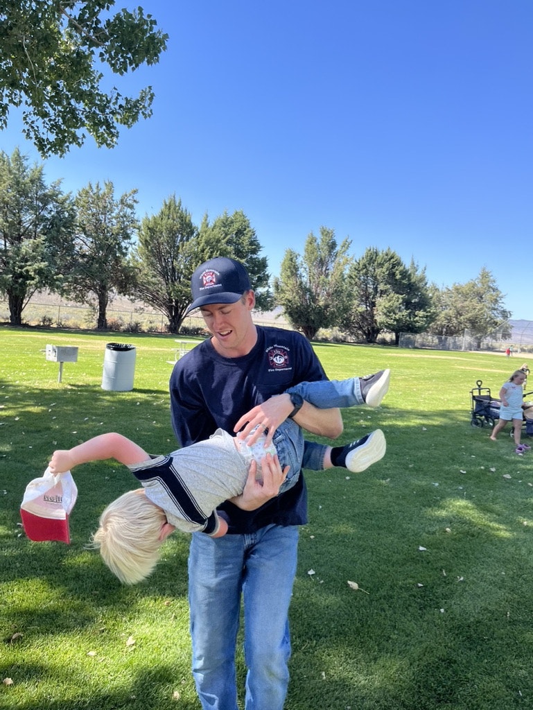 A man playfully holding a child upside down in a sunny park setting.