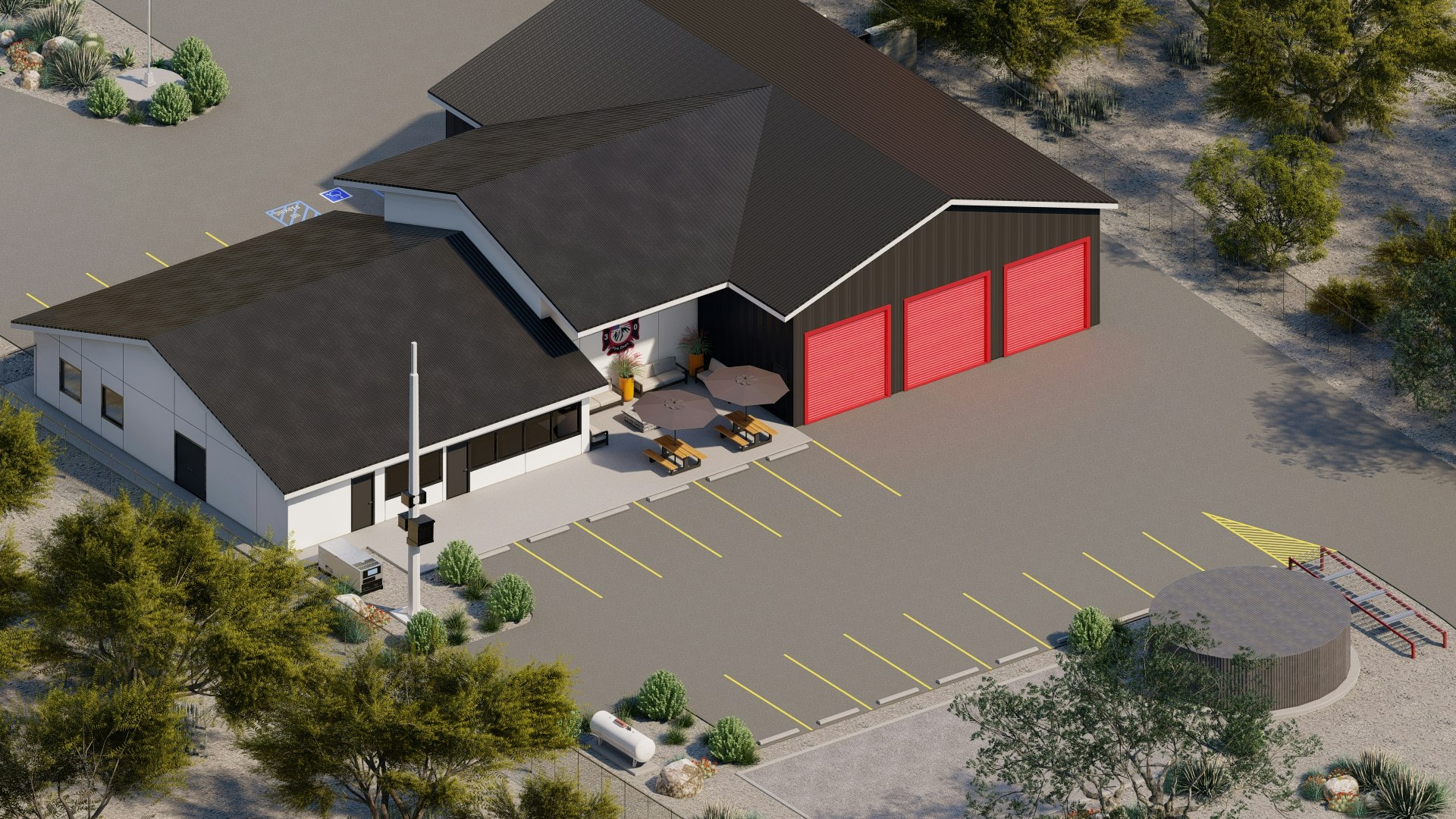 Aerial view of a building with red garage doors, picnic tables, umbrellas, parking spaces, and surrounding desert landscape.