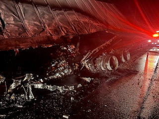 Overturned truck on a road at night with debris and red emergency lights visible.