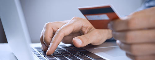 A person is using a laptop and holding a credit card, likely making an online purchase.