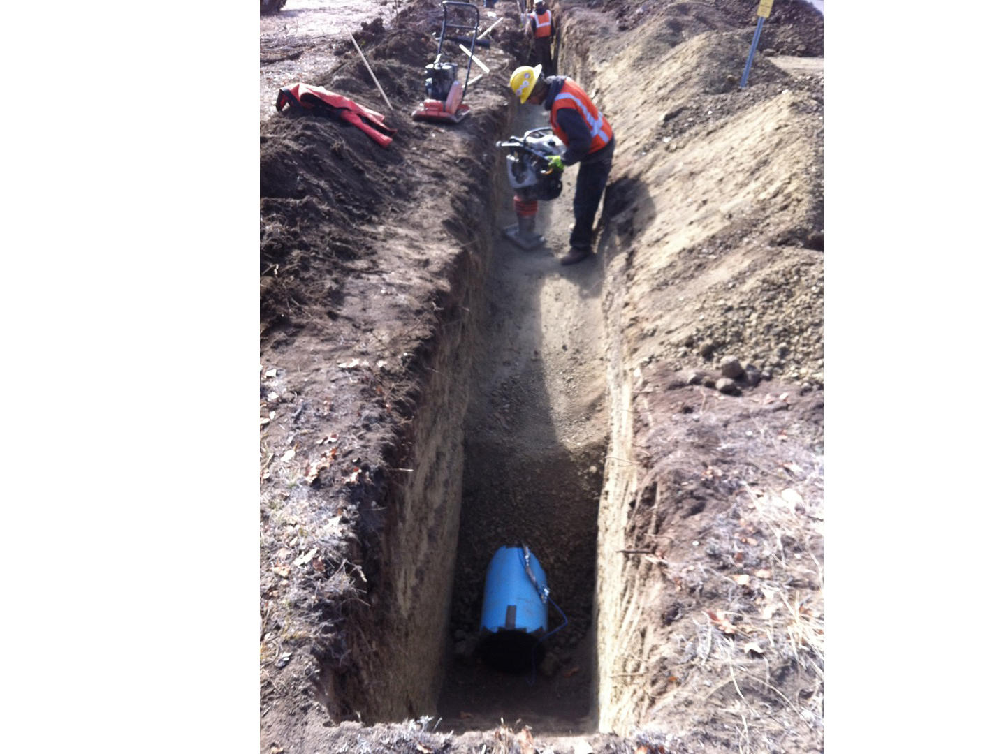 Construction workers in a trench installing a blue pipeline.