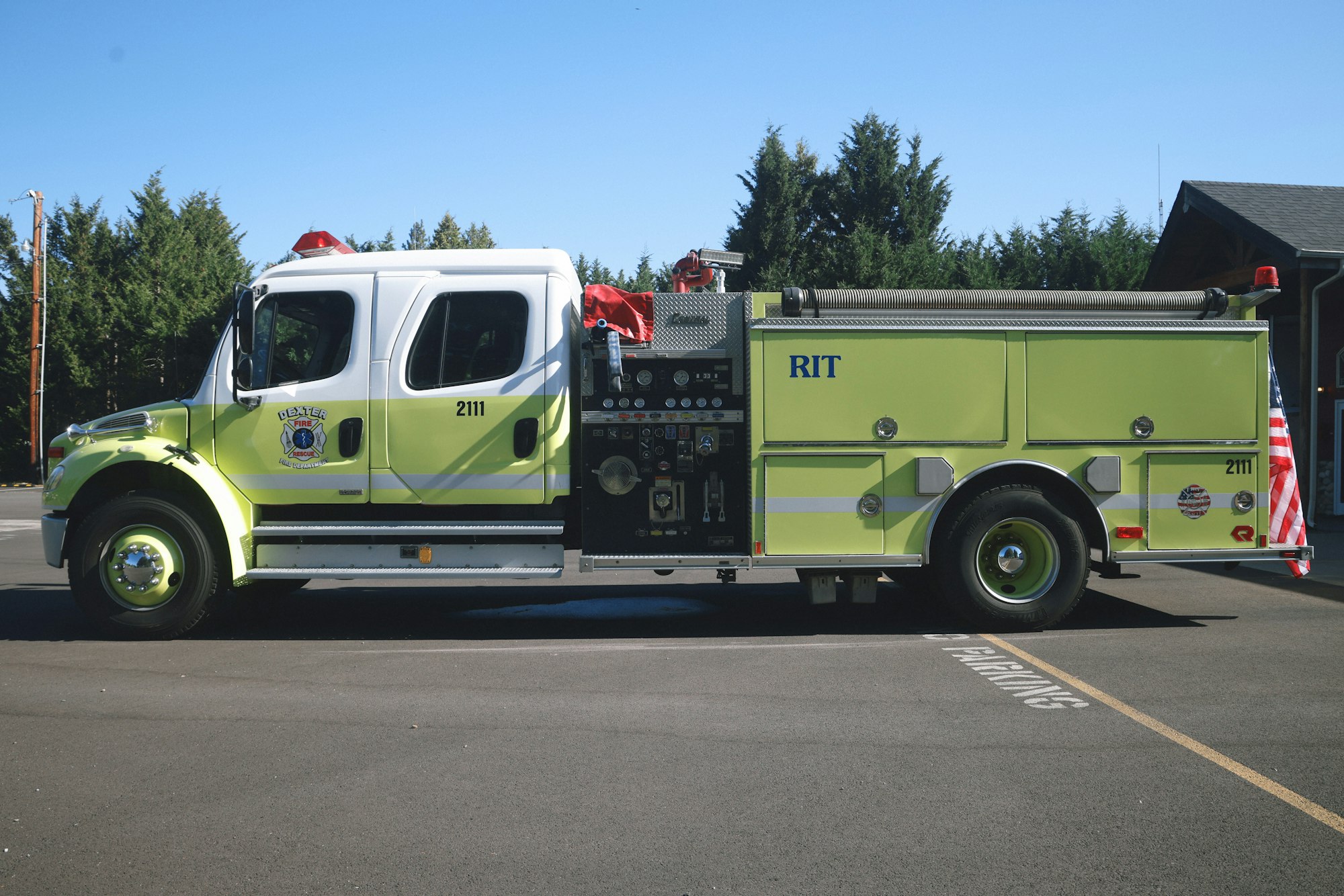 A green fire truck with "2111" and "RIT" visible, parked outside near trees on a sunny day.