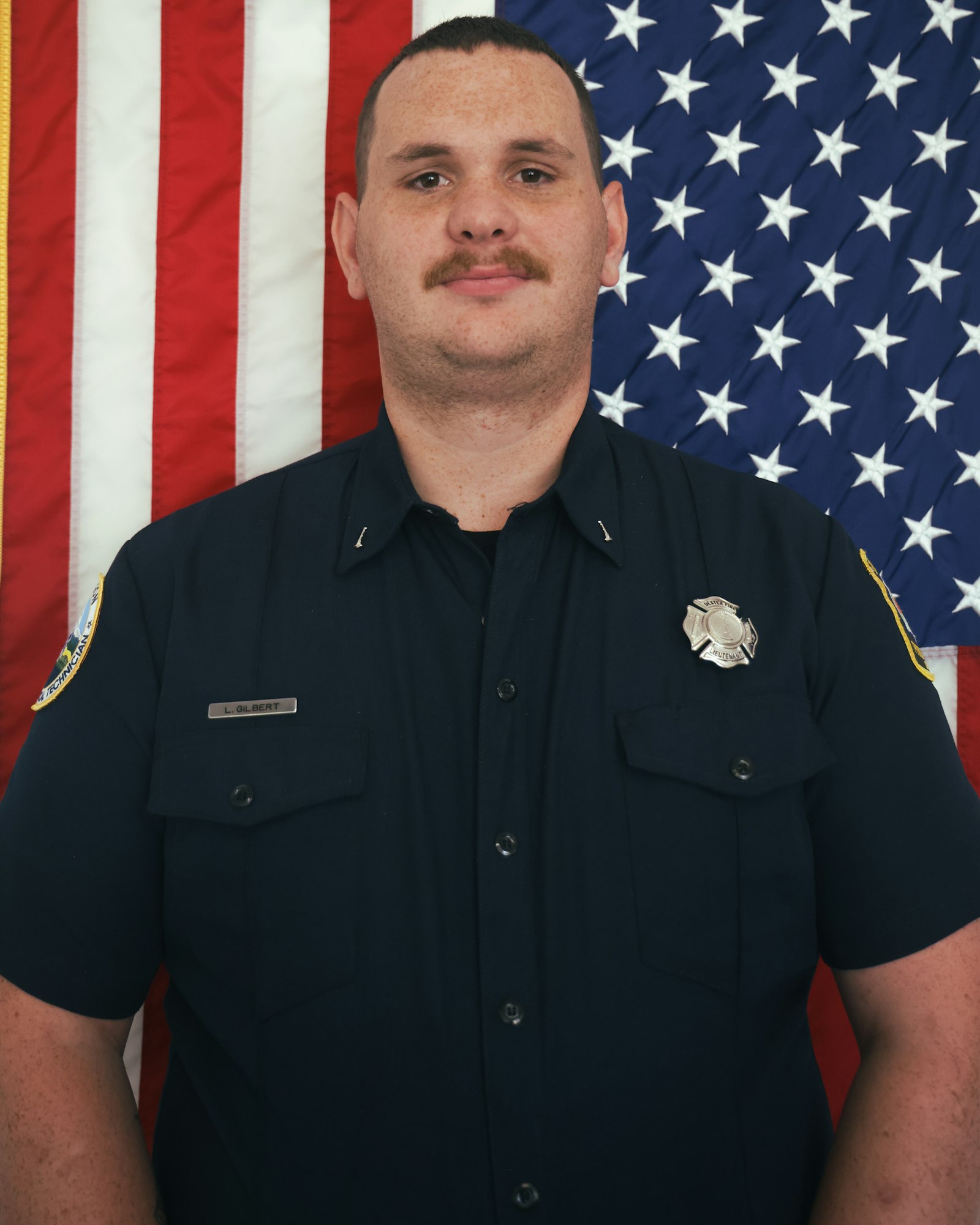 A person in a uniform stands in front of an American flag.