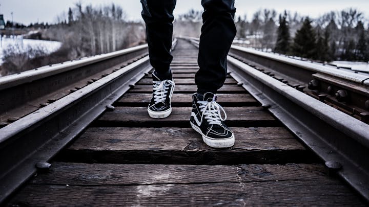 A person's legs walking on railroad tracks with snowy landscape in background.