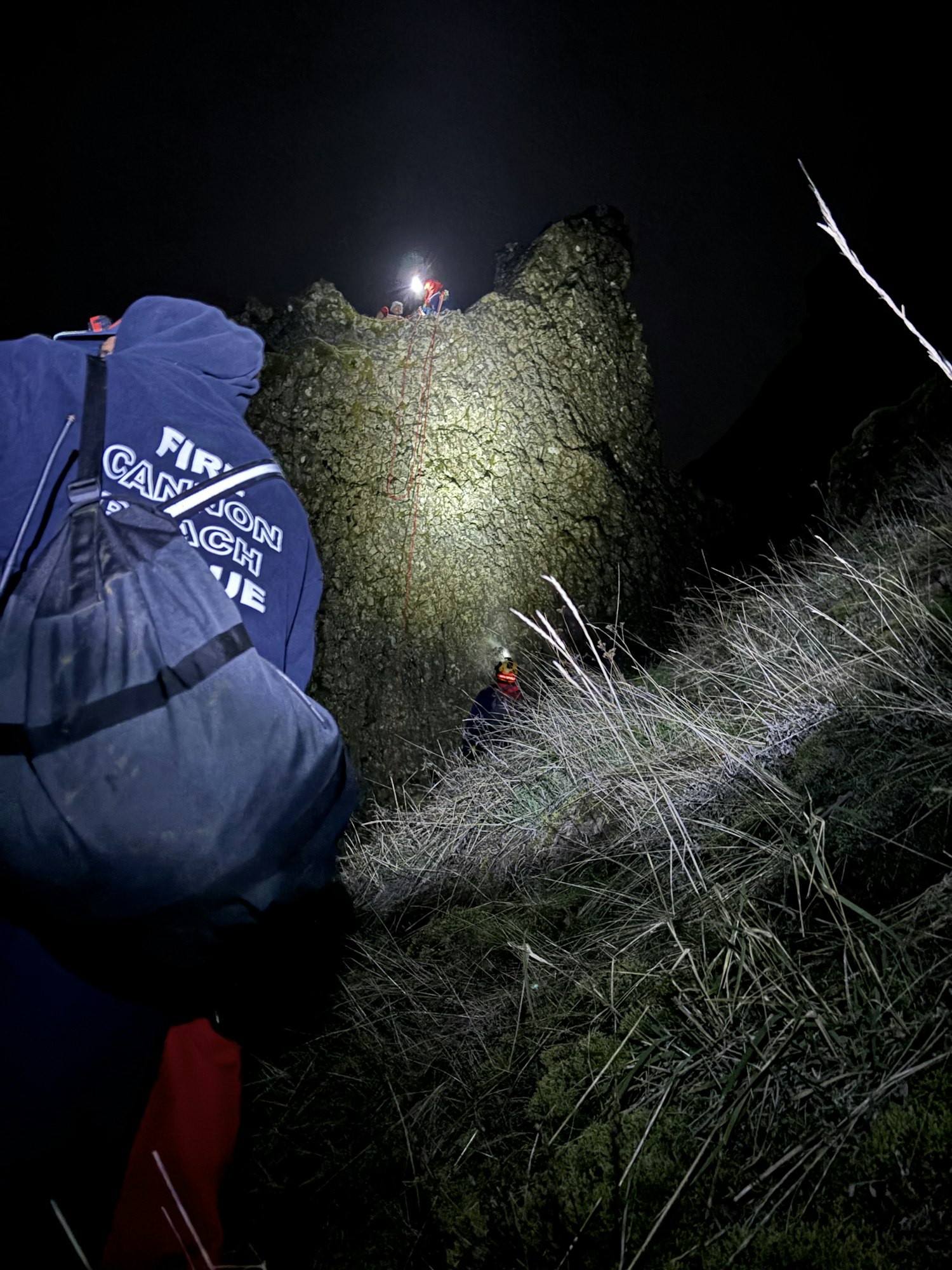 The image shows a nighttime scene with rescuers using lights on a rocky terrain, possibly during a canyoning or climbing activity.
