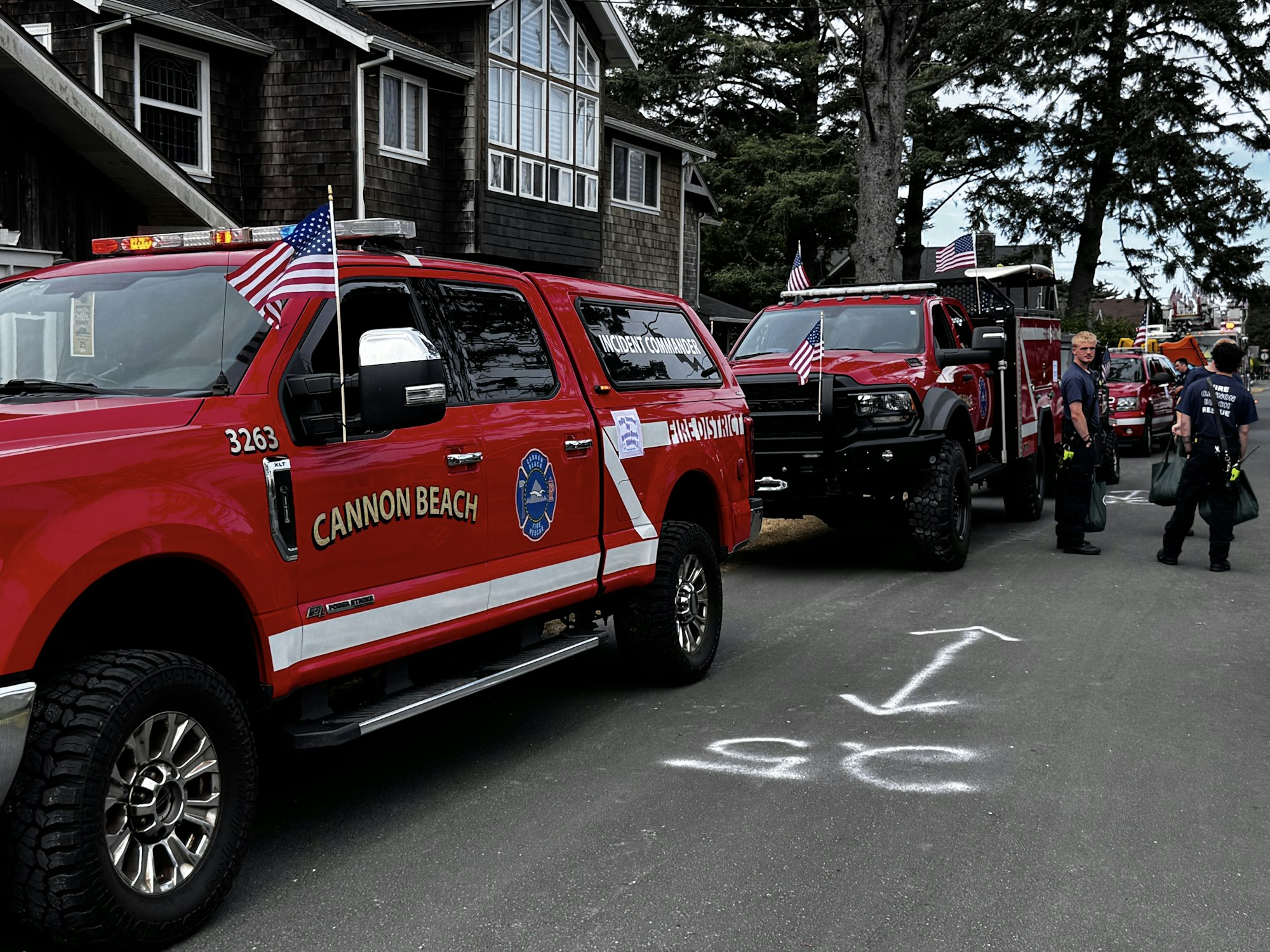 The image shows red emergency vehicles with American flags, parked on a street, alongside personnel preparing for a response.
