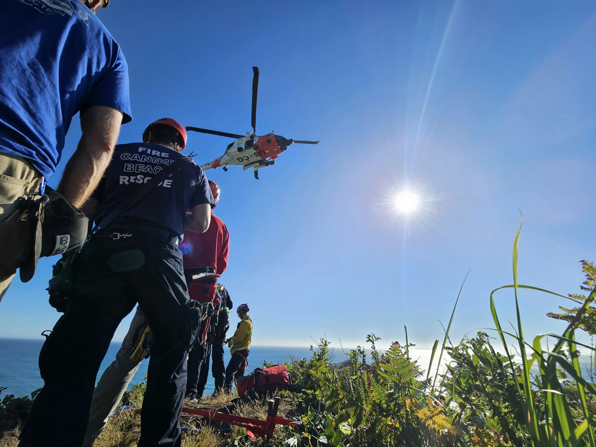 An upside-down viewpoint of climbers with gear and a helicopter against a clear blue sky.
