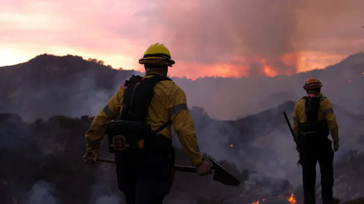 Firefighters in protective gear battle wildfires against a dramatic sunset backdrop with smoke rising in the air.
