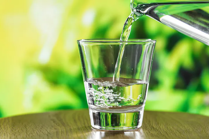 A glass is being filled with clear water, capturing the moment as bubbles form, set against a green background.