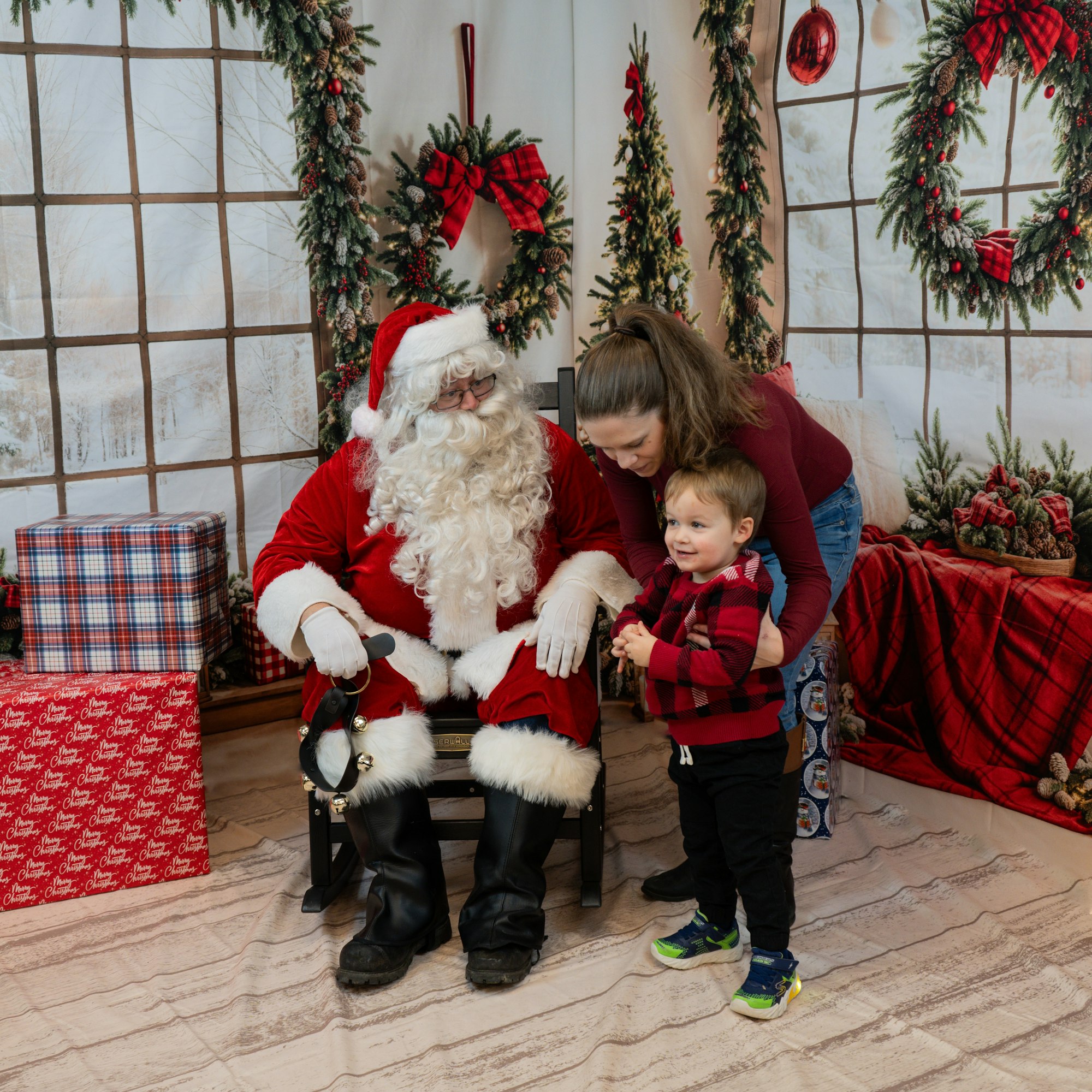 Santa Claus with a child and a woman in a Christmas-themed setting with gifts and decorations.