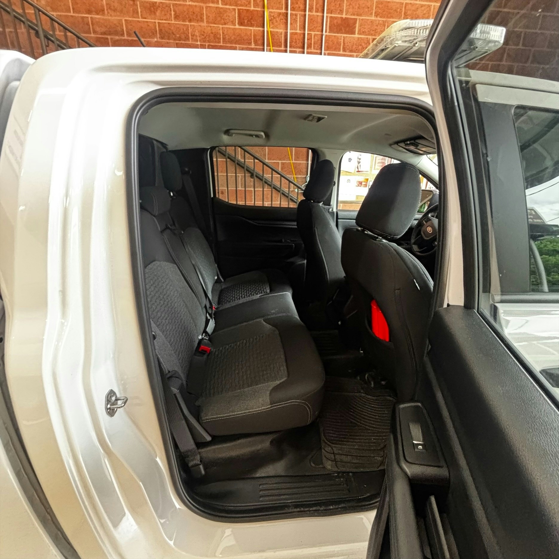 An interior view of a vehicle showing the back seat space and door, with visible seating and floor mats.