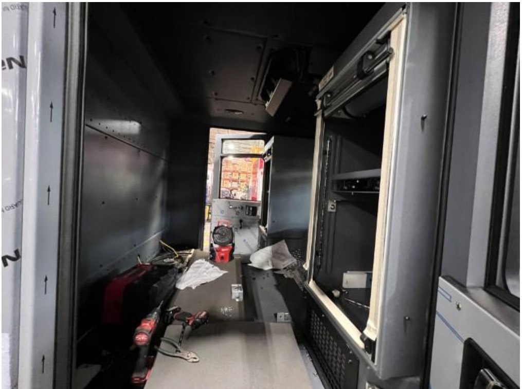 Interior of a partially assembled vehicle or industrial space with tools, shelves, and a window.