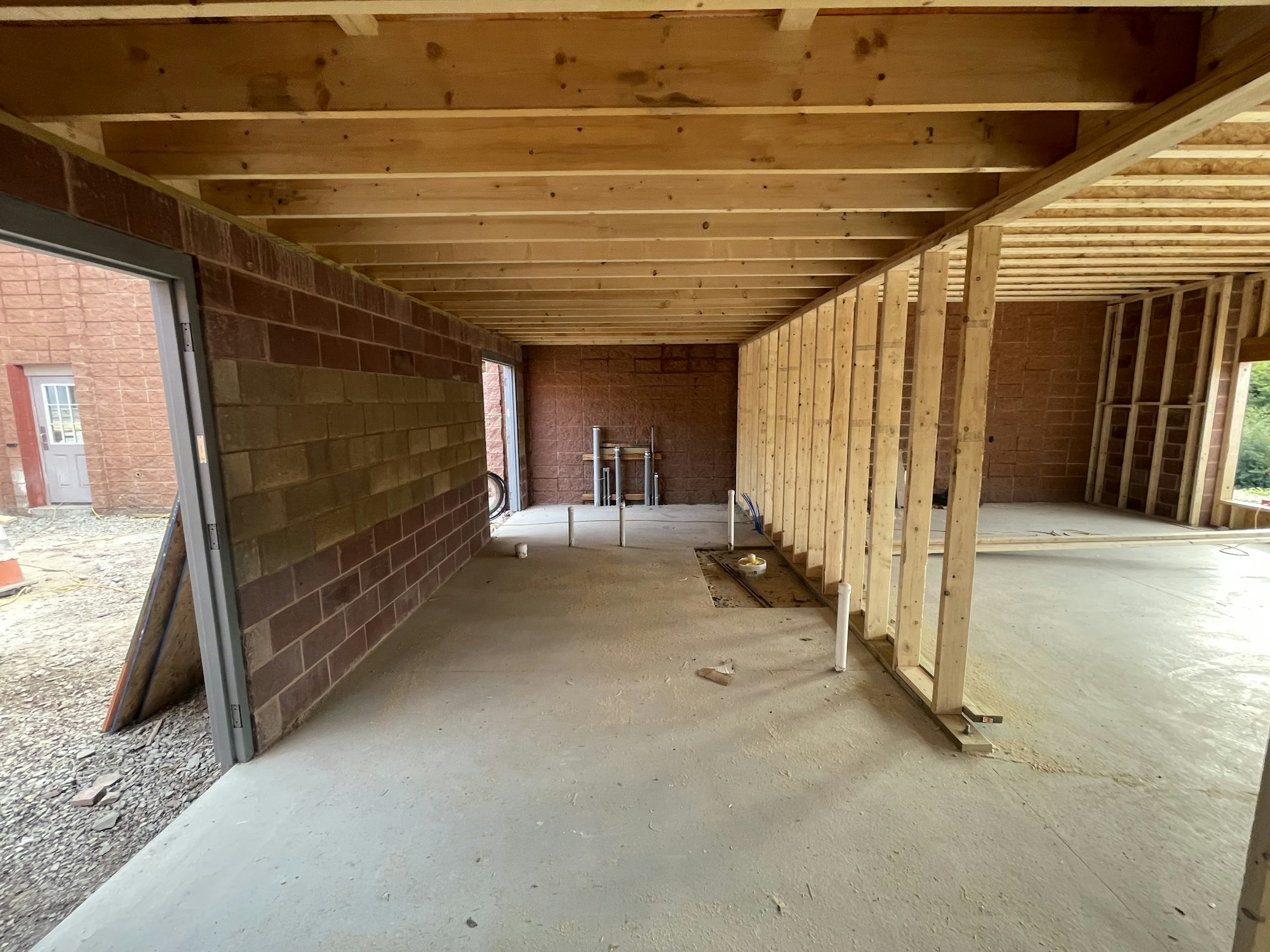 A partially constructed building interior with wooden framework, concrete floor, and brick walls.