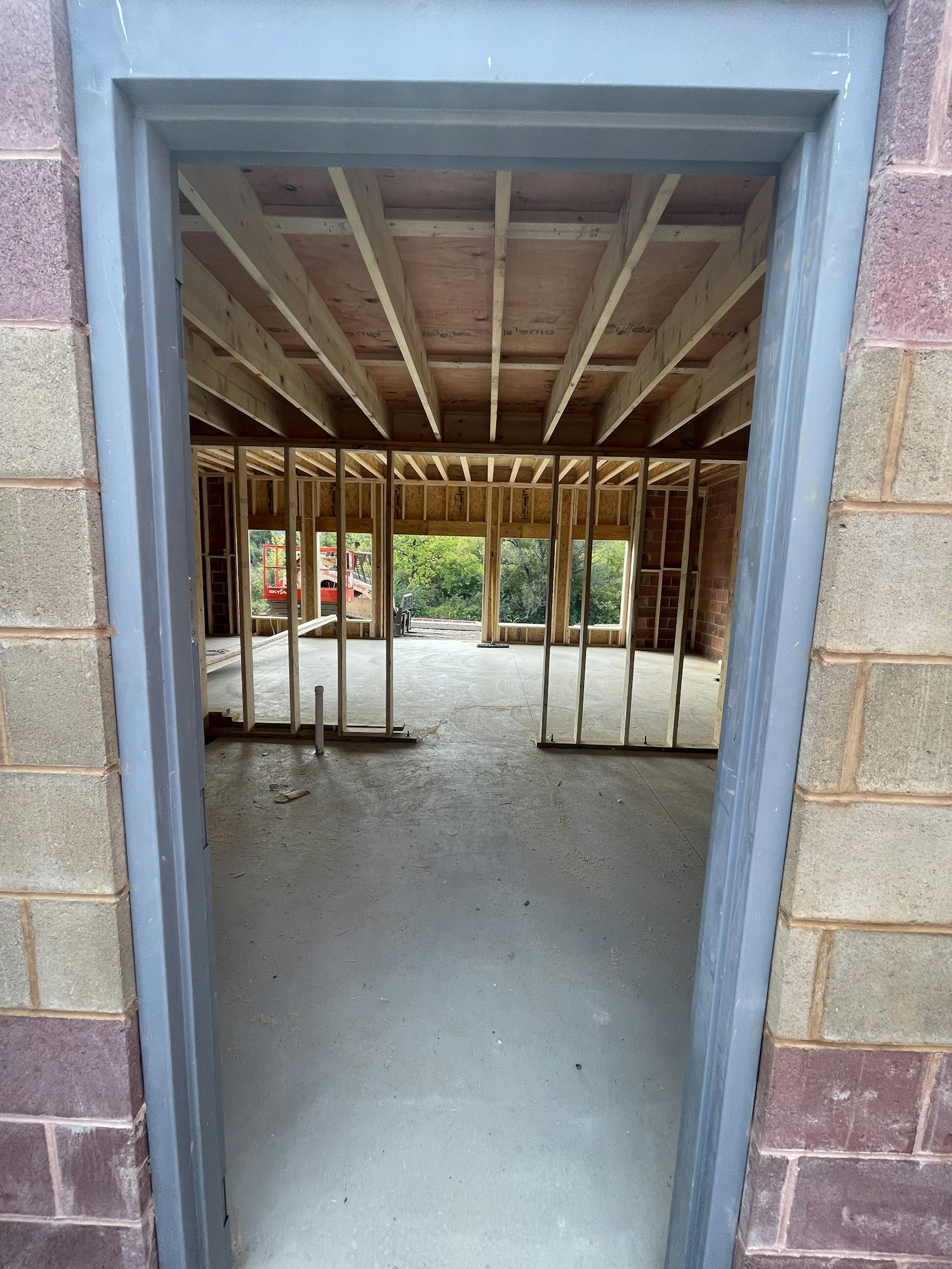 Interior construction site viewed through a window, with exposed wooden framing and concrete flooring.