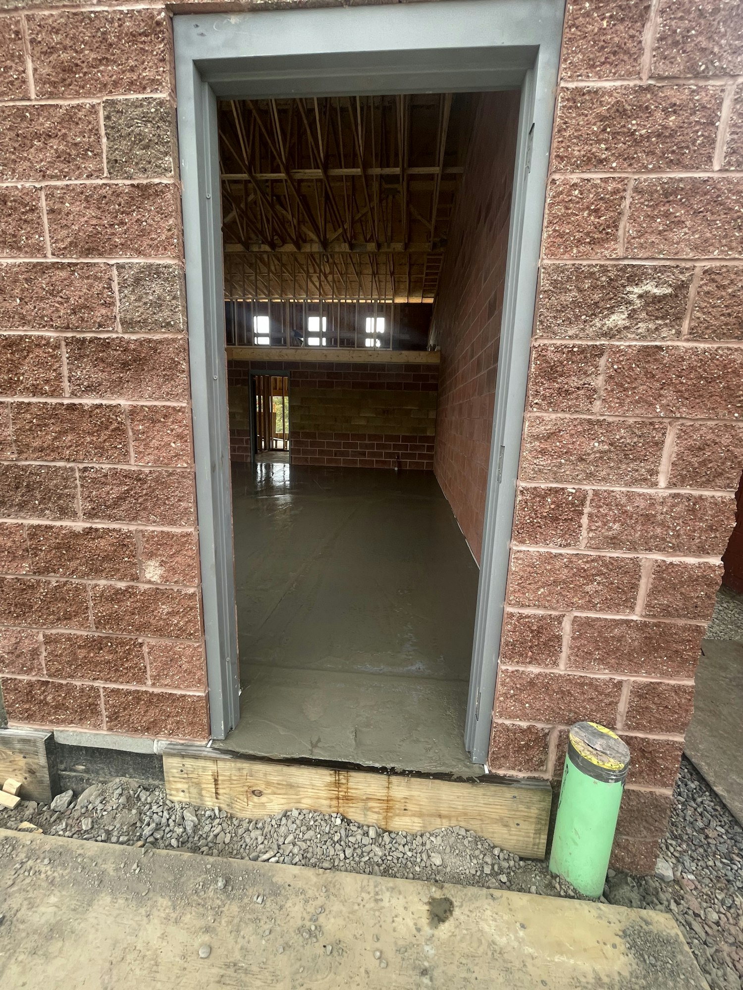 Construction site with a window, wooden scaffolding inside, green pipe outside, and brick facade. (The image is rotated clockwise.)