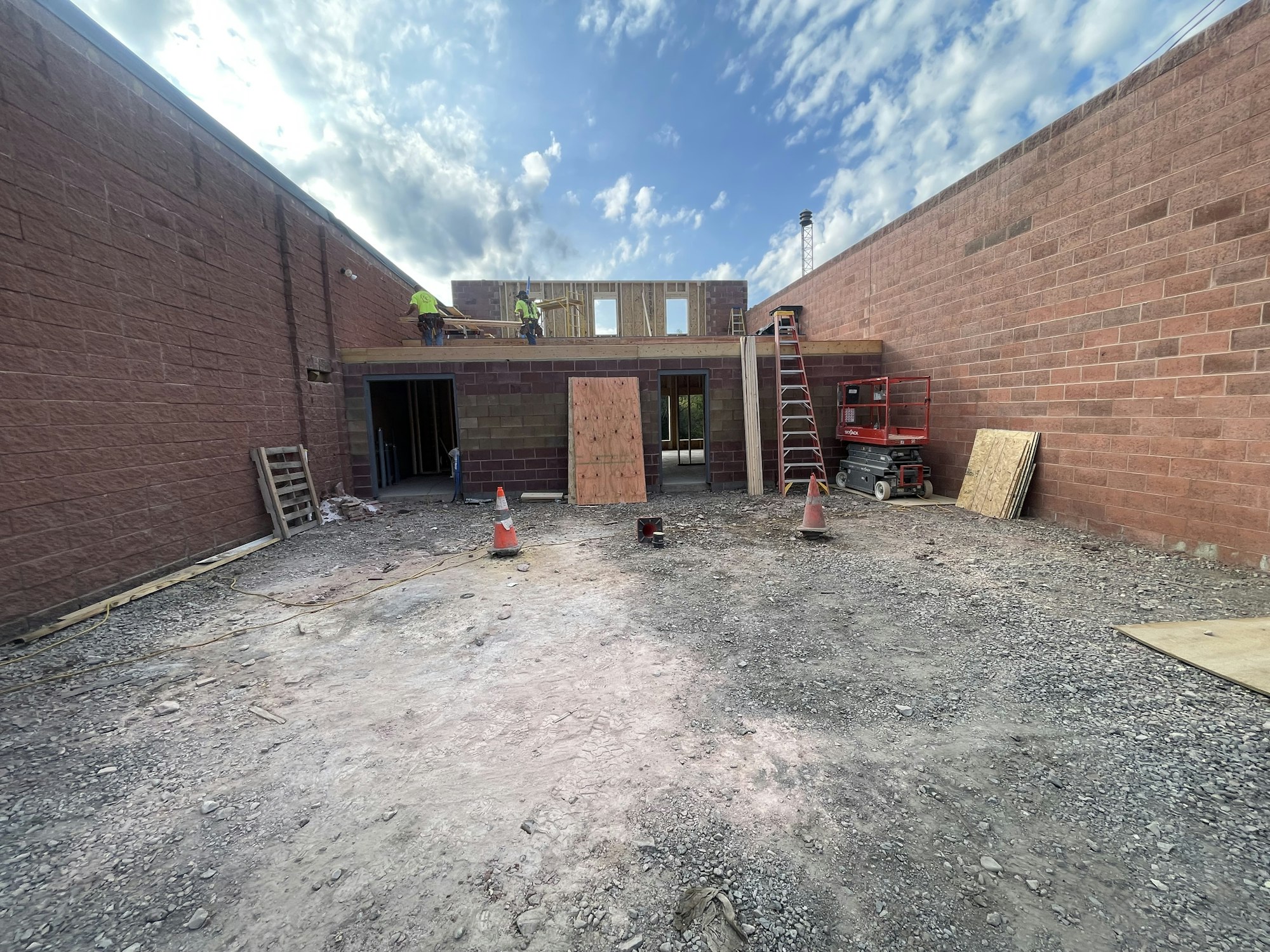 A construction site with workers, brick walls, and building materials under a cloudy sky.