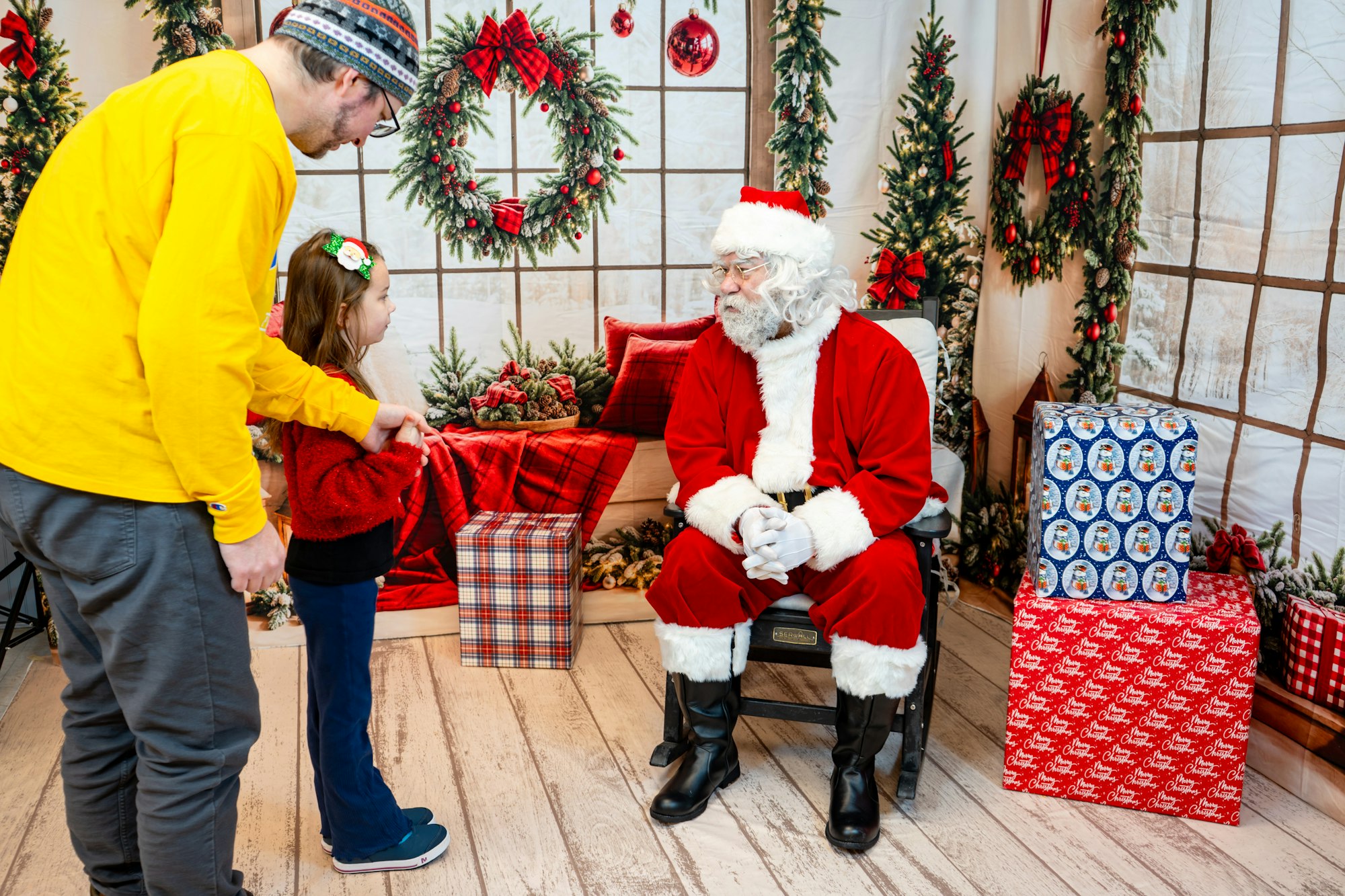 A child and adult are visiting Santa Claus amidst festive decorations and presents.