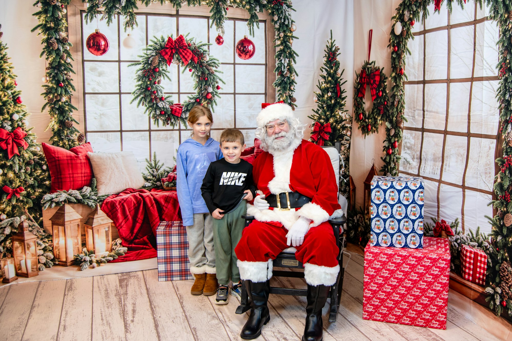 Children posing with Santa Claus in a festive holiday setting decorated with Christmas trees and gifts.