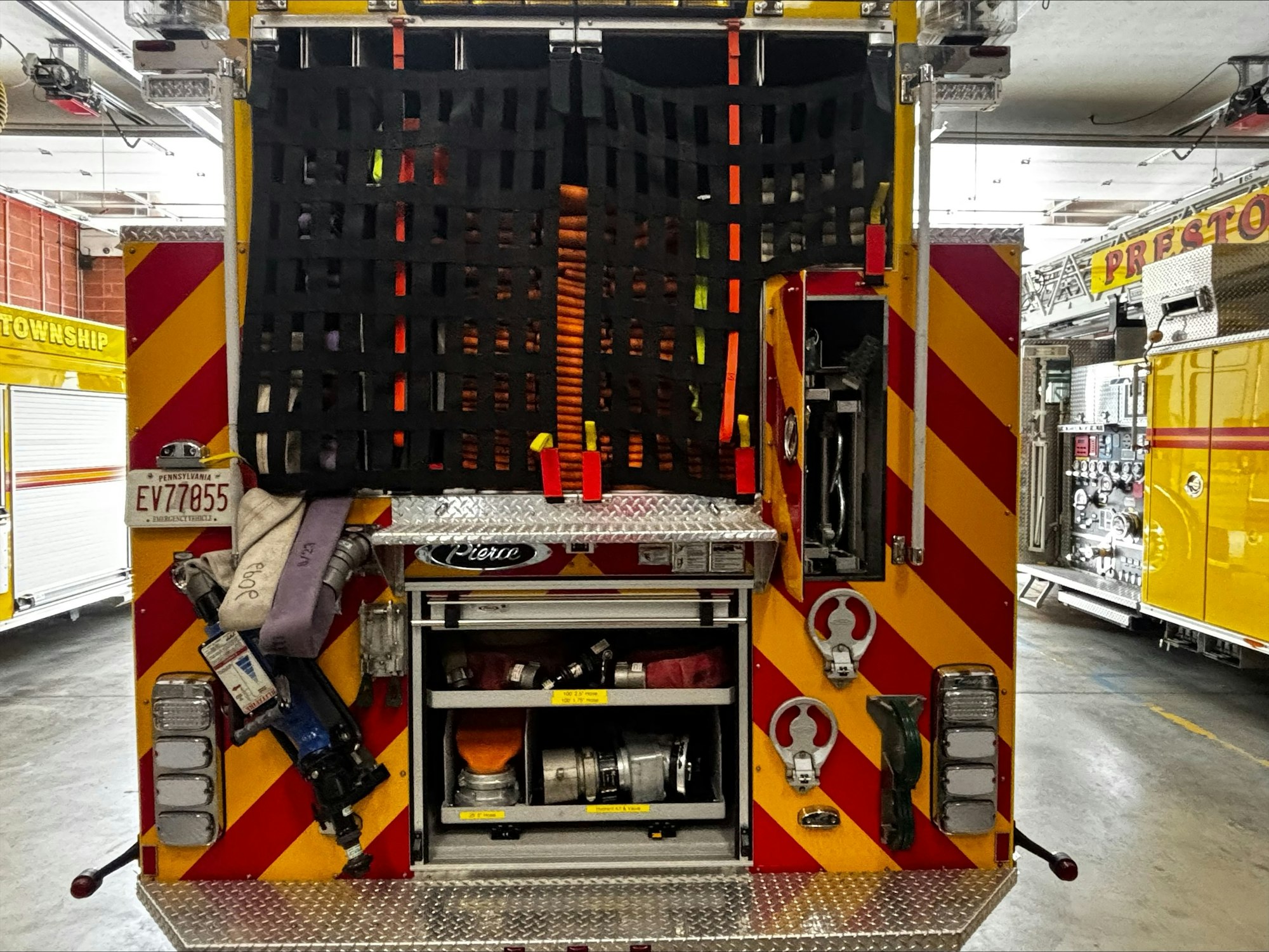 The back of a fire truck featuring storage compartments, tools, and a safety netting with bright colors.