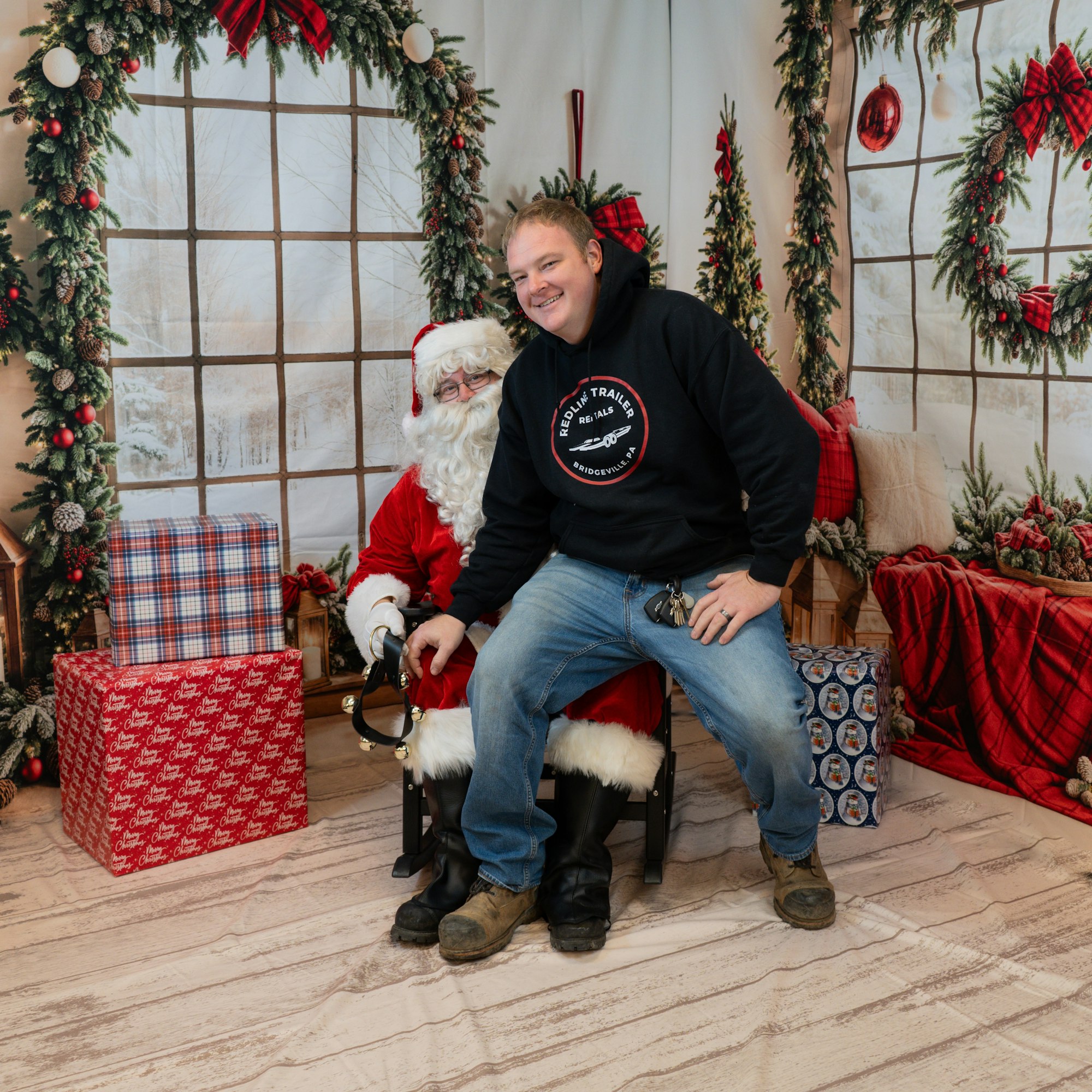 A person sitting with Santa Claus, surrounded by Christmas decorations and gifts.