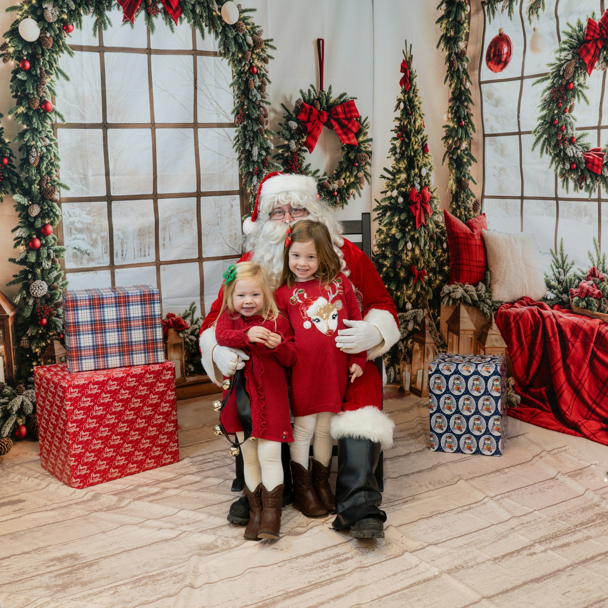 Santa Claus with two children in a festive setting, surrounded by Christmas decorations and gifts.