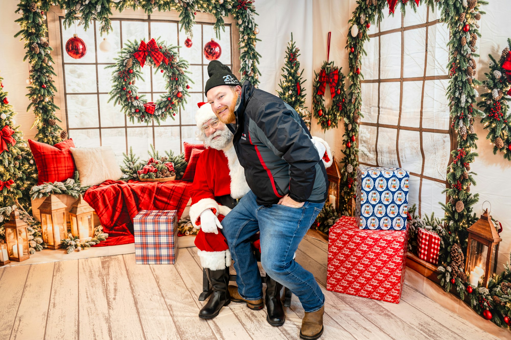 A man poses with Santa Claus in a festive holiday setting filled with decorations and wrapped gifts.