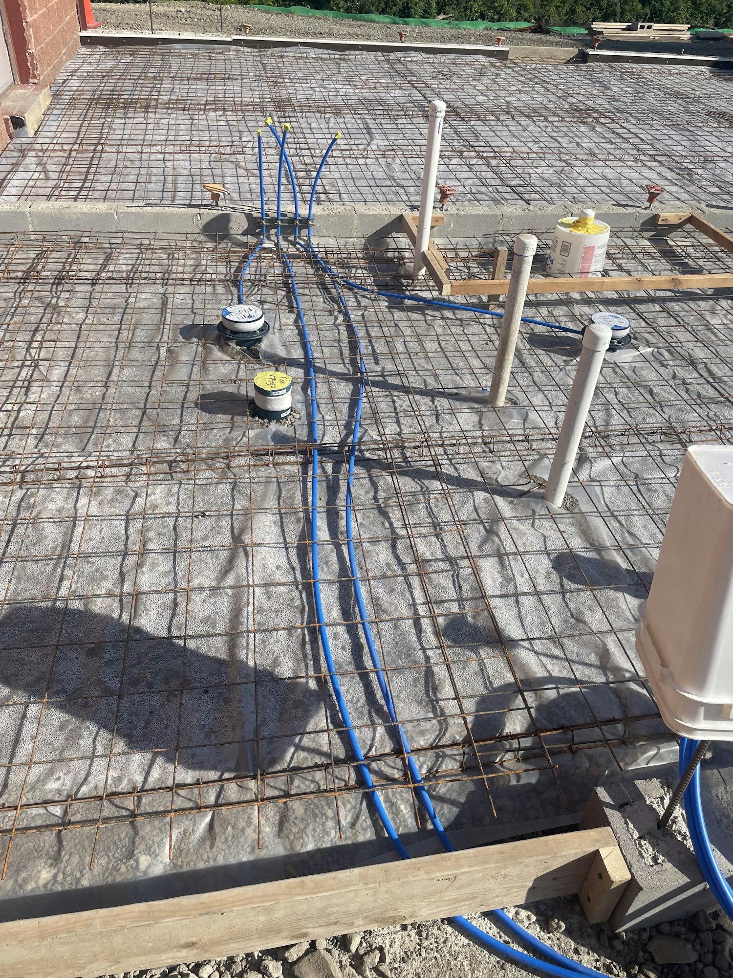 Construction site with rebar, plumbing pipes, and valves on concrete foundation, prepping for a pour.