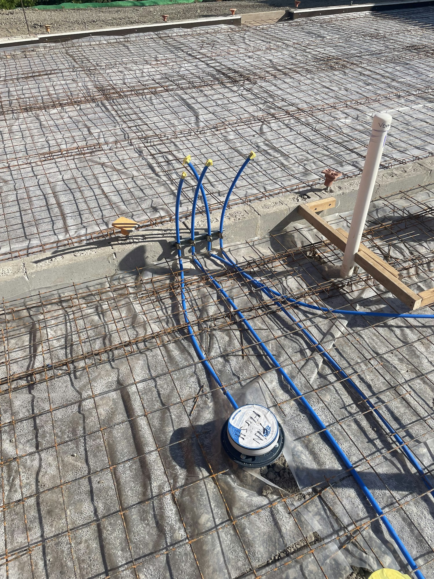 Reinforcement mesh with PVC pipework and an electrical floor box on a construction site.