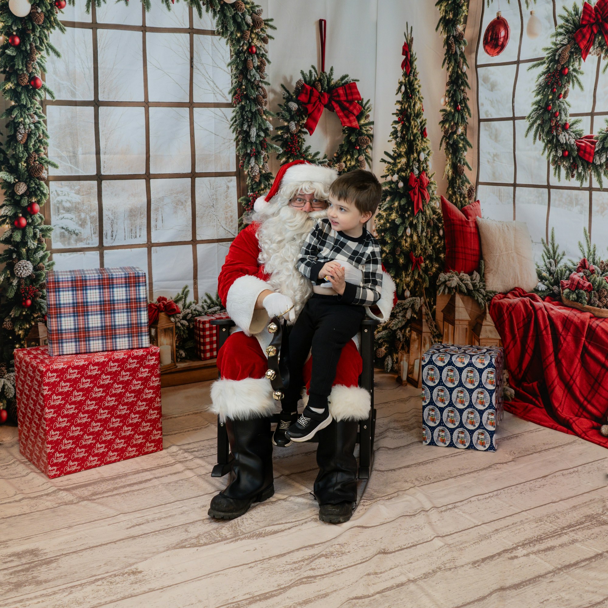 Santa and a child posing in a festive, holiday-themed room with gift boxes and decorations.