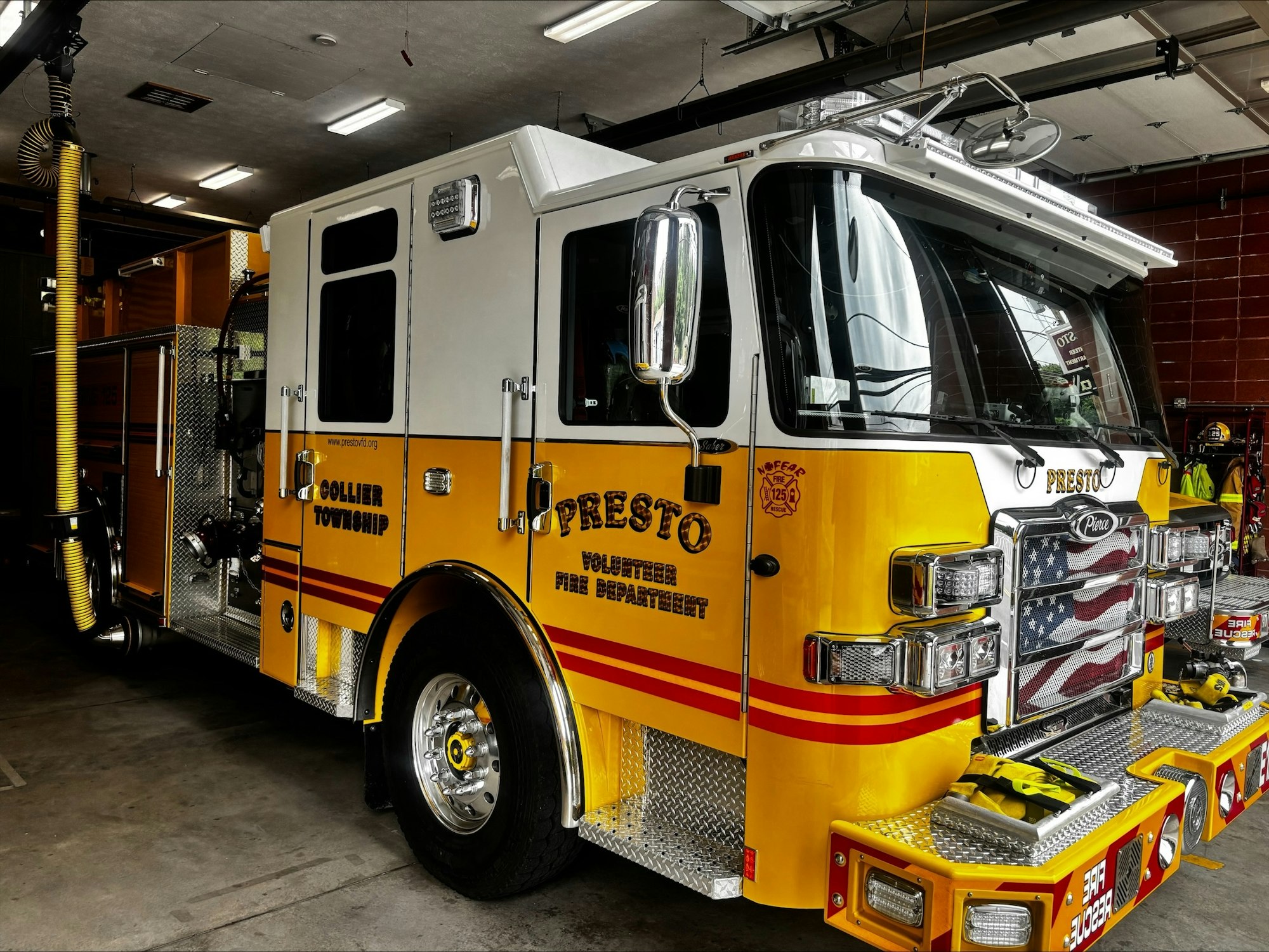 A yellow fire truck with "Presto Volunteer Fire Department" on its side, parked in a garage.