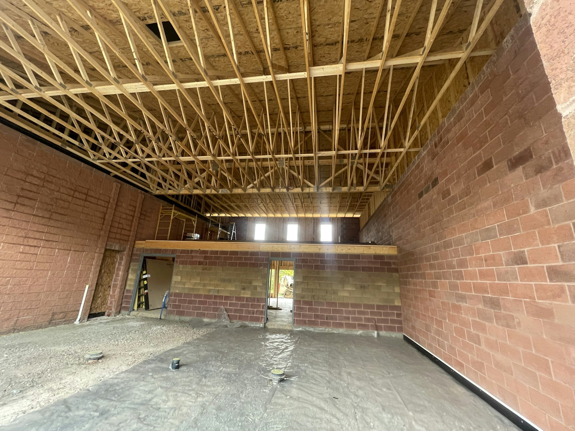Under-construction room with exposed wooden trusses, brick walls, and a dirt floor.