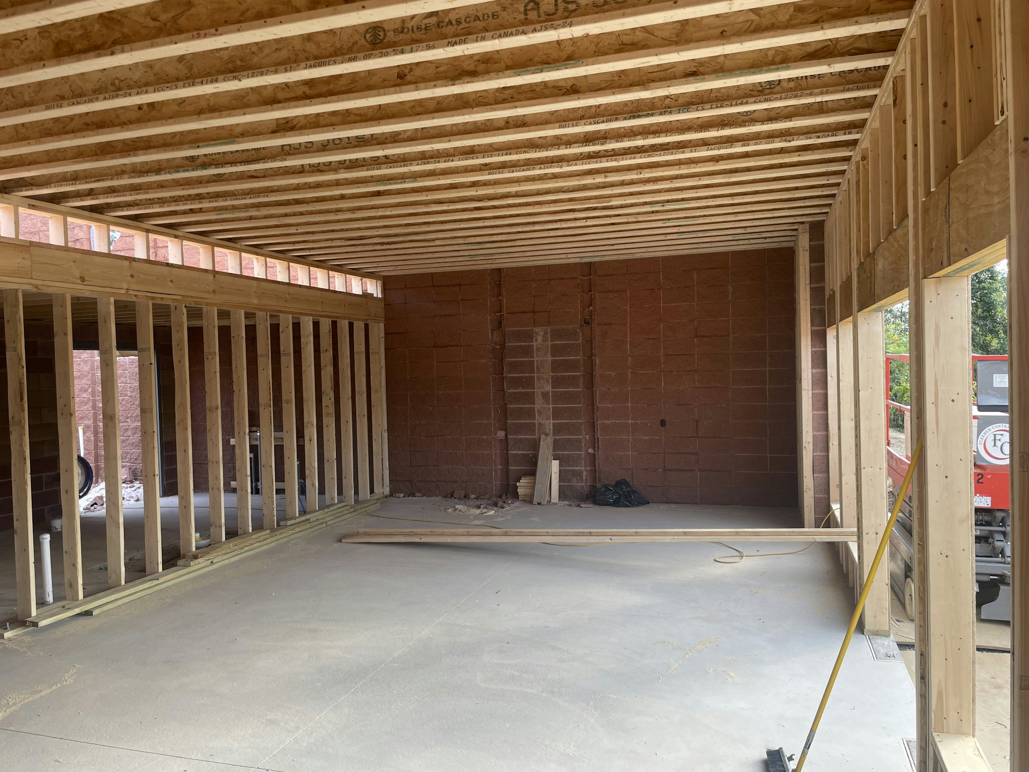 An unfinished interior of a building with exposed wooden studs and joists, concrete floor, and a brick wall.