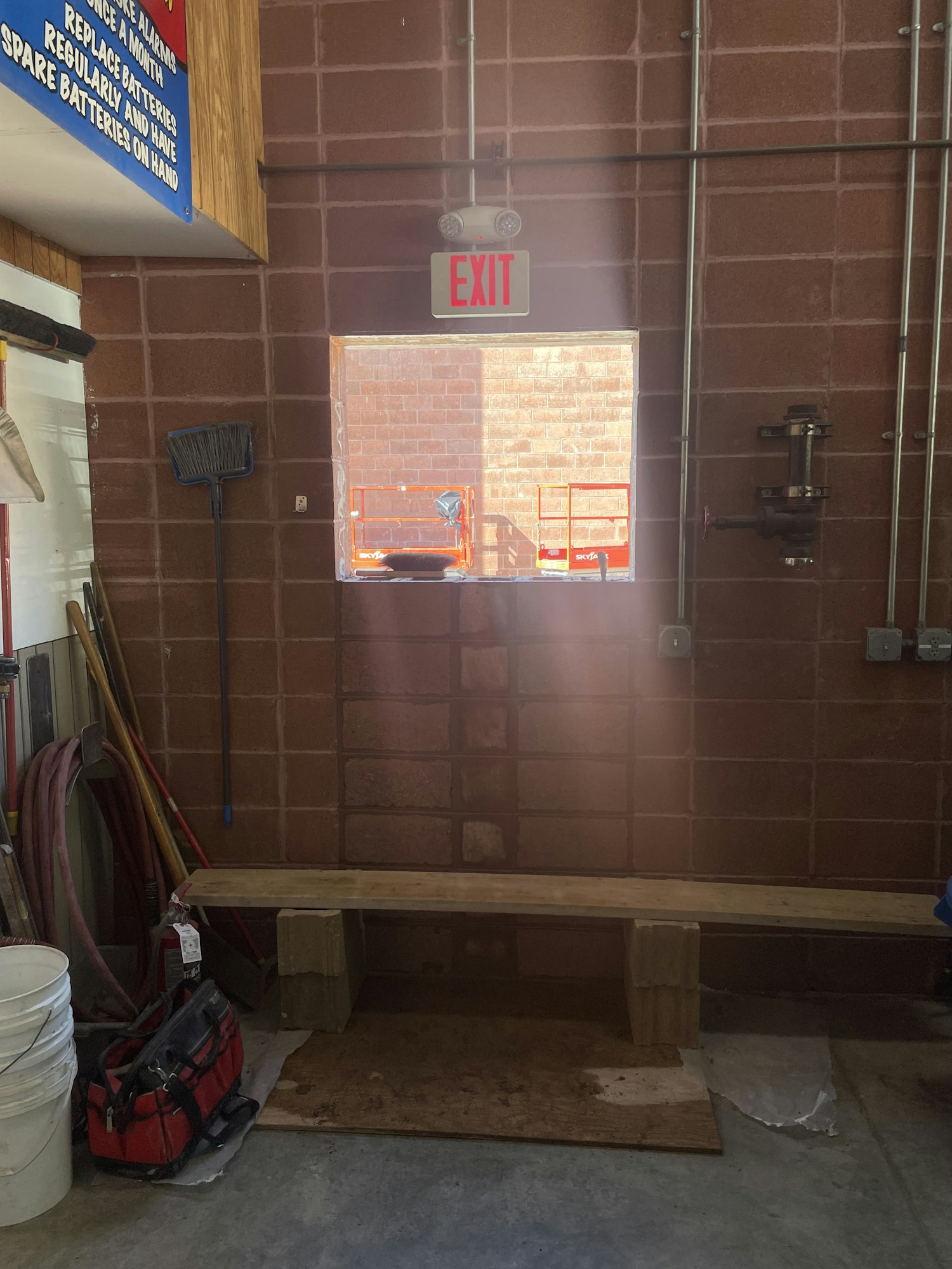A tilted image of a storage area with an EXIT sign, tools, wooden shelving, and a view of the outside through a door.