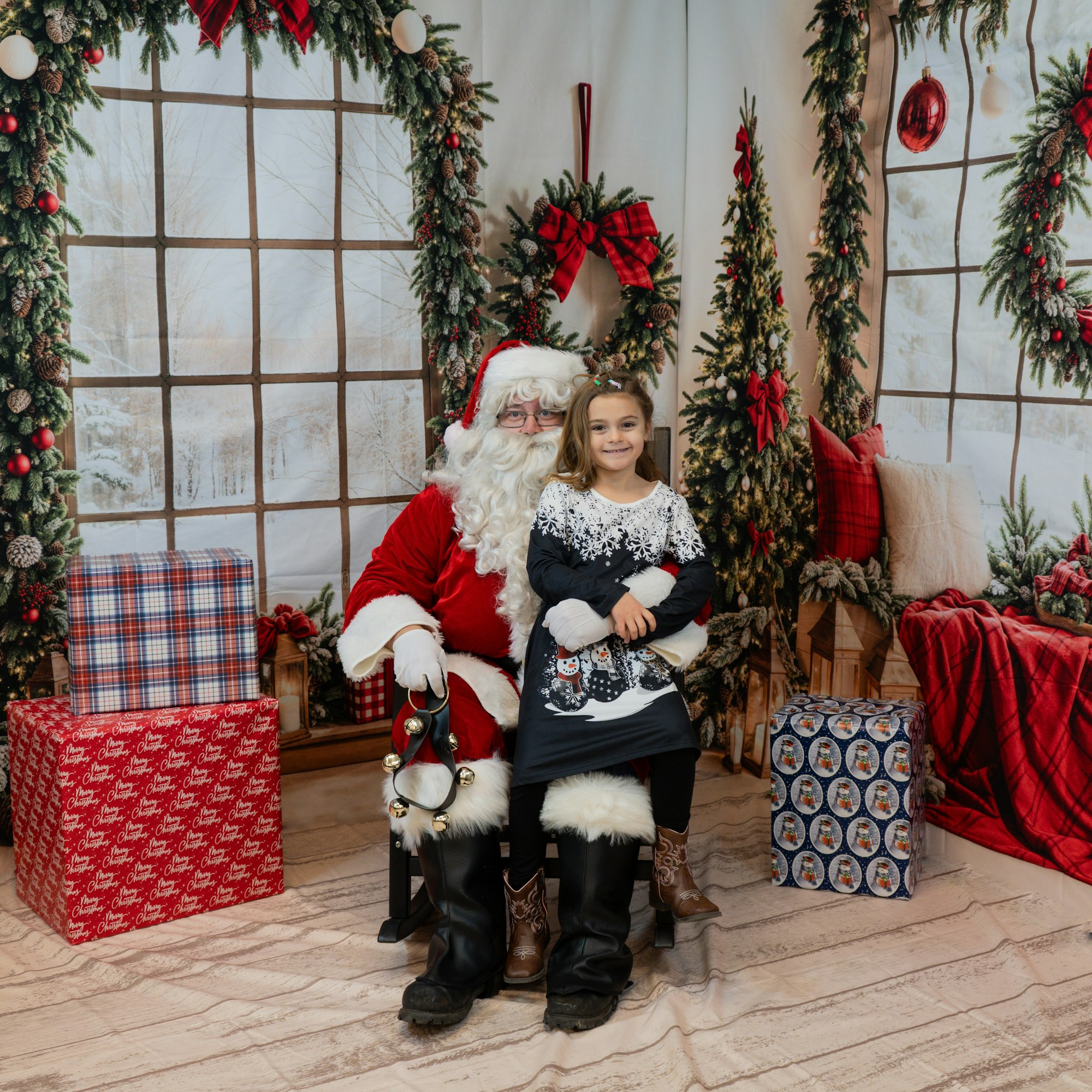 Santa Claus and a child pose in a festive setting with Christmas decorations and wrapped gifts.