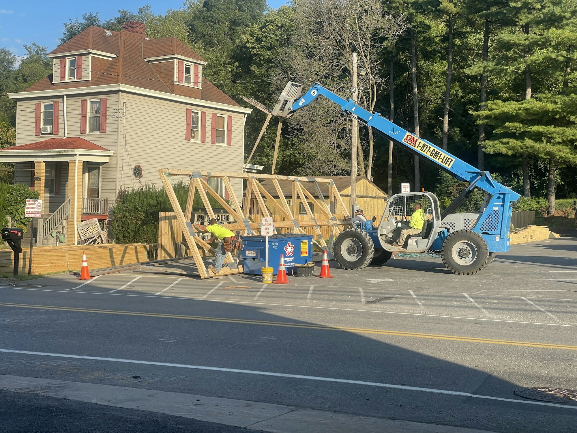 Construction work in progress with telehandler and wooden frames on a street near a house, and a worker visible.