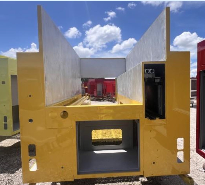 A yellow industrial structure with open sides and a central compartment, set outdoors under a blue sky.