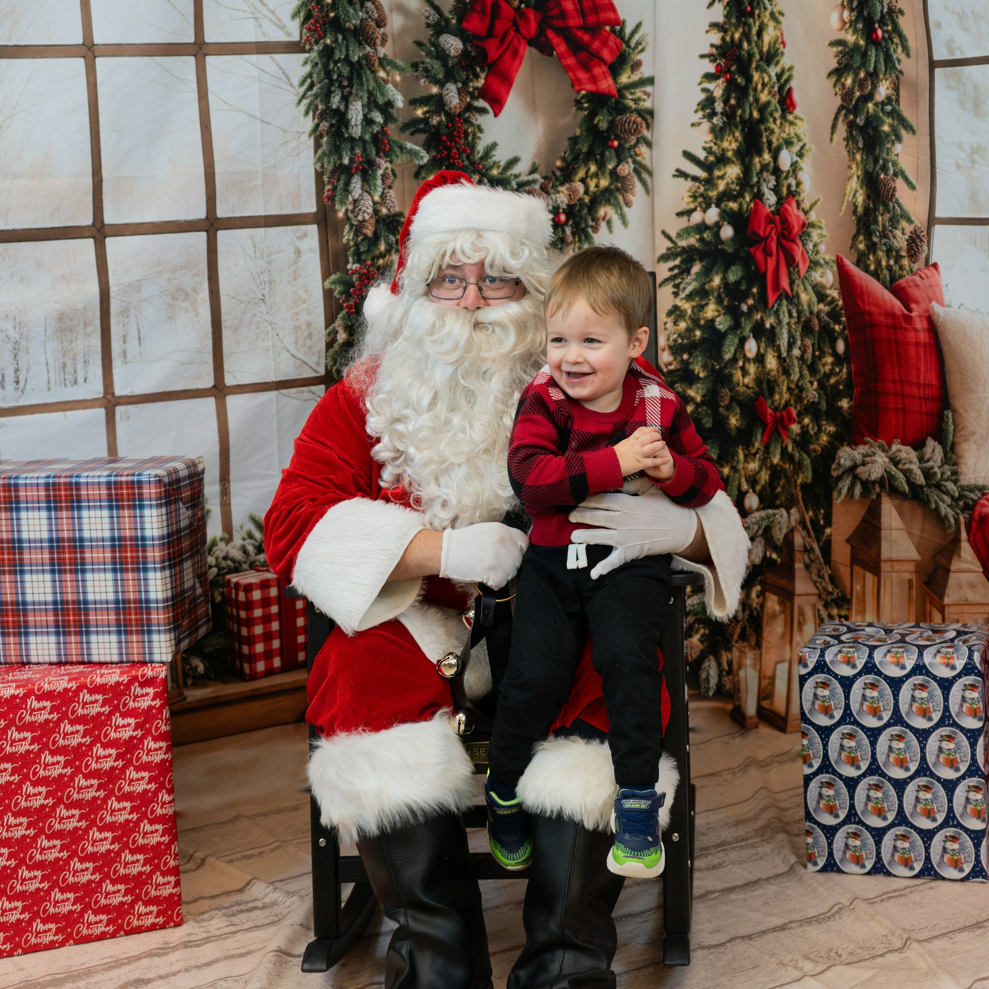 Santa holding a smiling child with Christmas trees and gifts in the background.