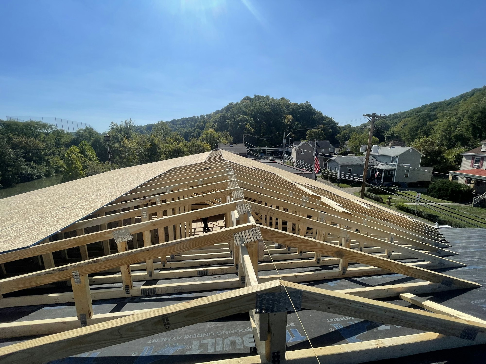 New roof trusses on a building under construction, with a clear sky and neighborhood in the background.