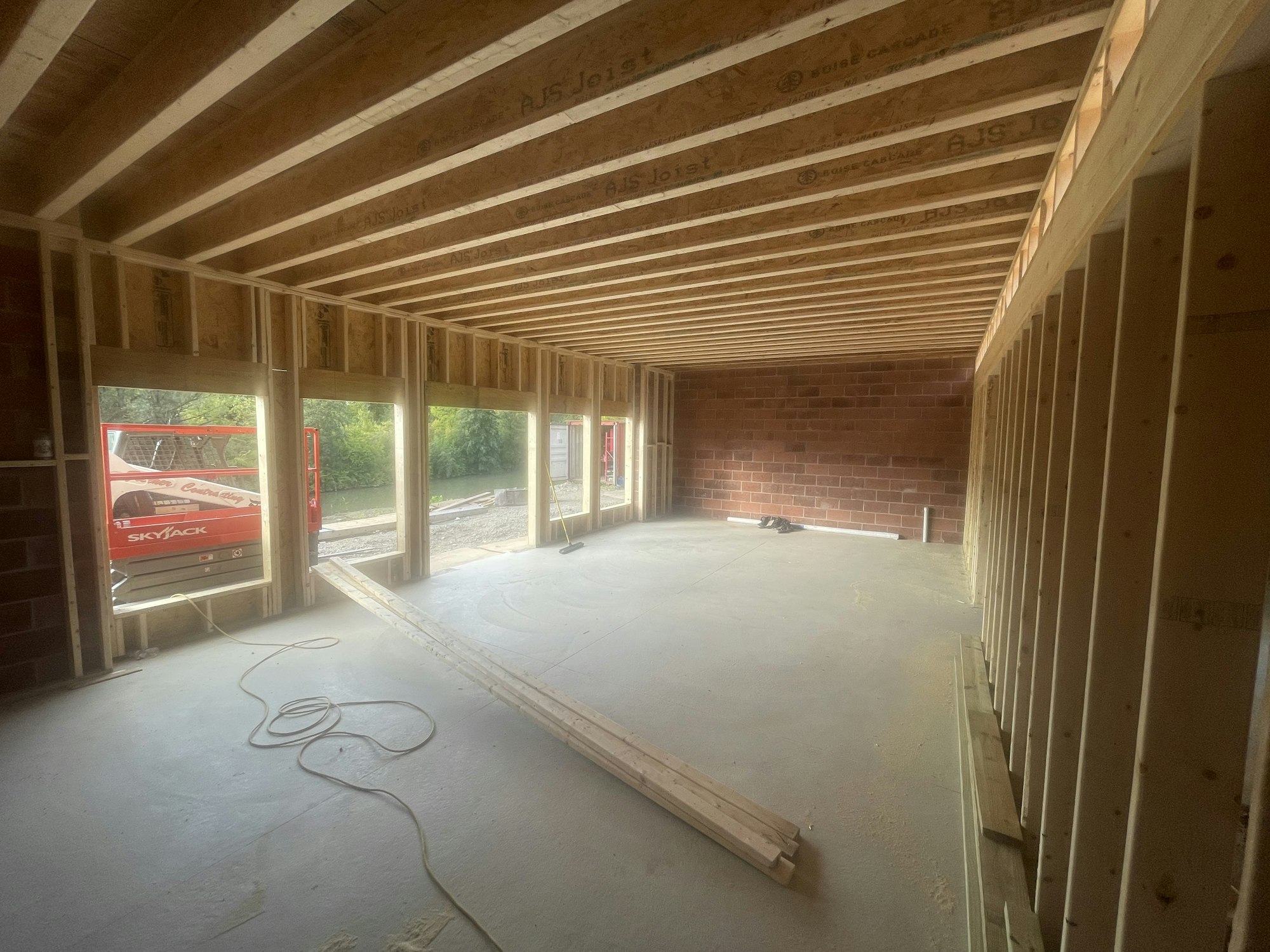 An unfinished interior space with exposed wooden framing, brick walls, and a scissor lift visible through an open doorway.